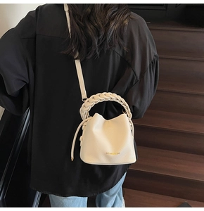 Detail of off-white leather bucket bag with woven handle on dark wooden stairs