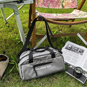 Gray grid texture crossbody sports bag with black handles on a scenic outdoor lawn