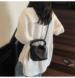 Detail of black lychee grain leather bucket bag with woven handle and gold logo lettering