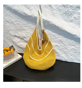Detail of hollow woven straw beach bag with yellow stripes and red strawberry pendant