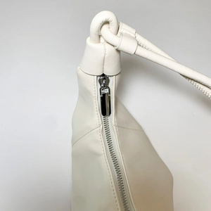 Detail of minimalist cream leather handbag with knotted strap and silver metal zipper