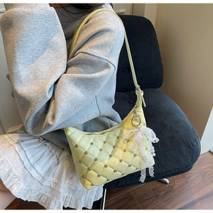 Close-up of quilted yellow underarm bag with silver rivets and lace pearl bow detail