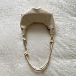 Detailed close-up of cream croissant shoulder bag featuring unique vertical pleats and knot