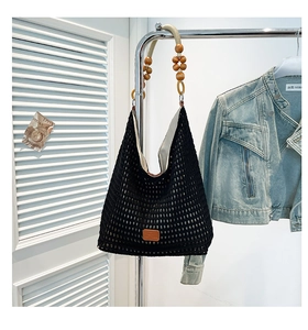 Detail of black woven mesh tote bag featuring decorative wooden beads and a small leather patch