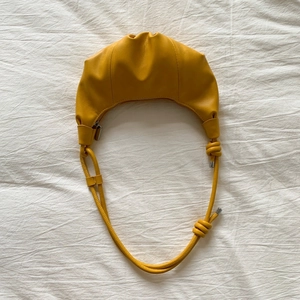 Top view of a bright yellow leather croissant bag with knotted strap details on white fabric