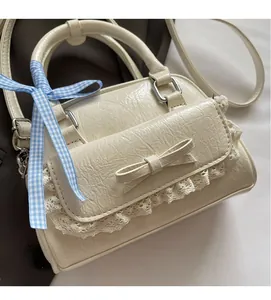 Detailaufnahme einer cremeweißen Schleifenhandtasche mit Spitzenbesatz und weichem Kunstleder