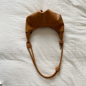 Detail of caramel crescent crossbody bag with pleated texture and knot strap accents