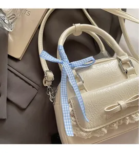 Detailansicht der cremefarbenen Ledertasche mit Spitzenbesatz und blau karierter Schleife