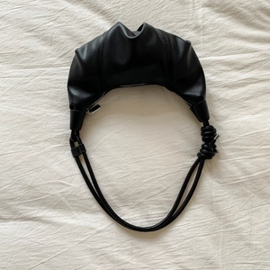 Close-up of black leather croissant bag featuring pleated texture and knot shoulder strap