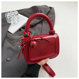 Dettaglio della borsa rossa in vernice con decorazione a fiocco e tracolla a catena di perle