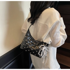 Close-up of black quilted hobo bag with silver studs and a pearl lace bow charm