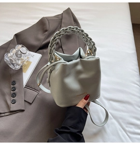 Detail of sage green bucket bag with braided handle on a suit and white bedding