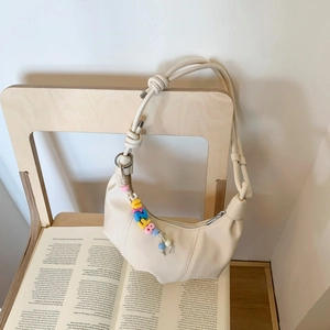 Detail of cream crescent moon bag featuring a thick twisted knot strap and letter charms