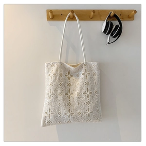 Dettaglio della borsa tote in pizzo bianco con motivi floreali traforati e manici in pelle