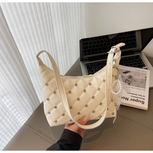 Close-up of quilted cream shoulder bag with metal studs and pearl lace charm