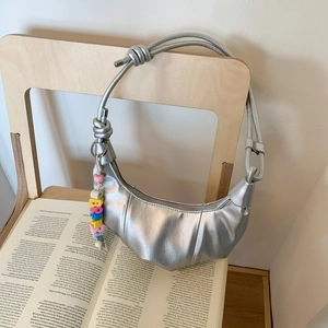 Detail of silver crescent shoulder bag featuring a knotted strap and colorful birthday bead charm