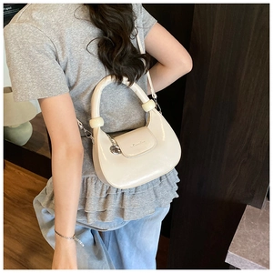 Detail of a creamy white crescent leather bag with puffy handle and metal charm