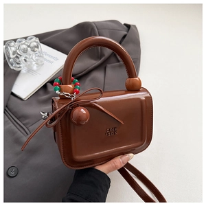 Dettaglio borsa a mano marrone lucida con fiocco elegante e ciondolo a perline chic