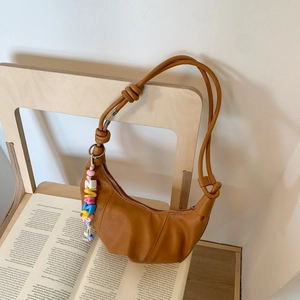 Detail of warm brown crescent bag with pleated leather texture and beaded charm decor