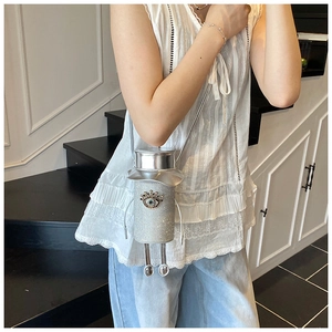 Detail of creative silver glitter cylindrical crossbody bag with eye-shaped crystal emblem