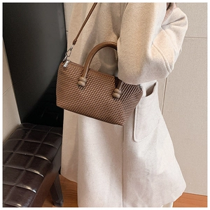 Detail showing brown woven texture of a stylish crossbody bag with rounded handles