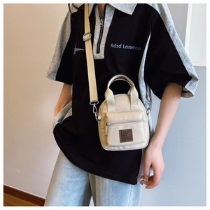 Detail of beige nylon crossbody bag featuring top handle and adjustable shoulder strap