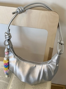 Silver metallic croissant bag with knotted strap and rainbow bead charm on wood chair