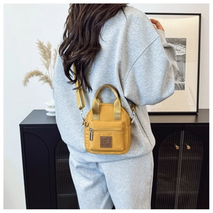 Model showing a yellow nylon mini crossbody bag with a front zipper pocket and adjustable strap