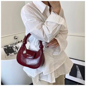 Detail of burgundy crescent moon bag featuring a knot handle and glossy finish on model