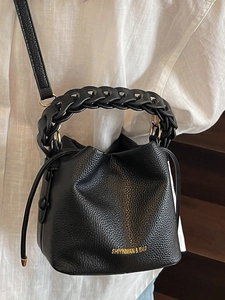 Classic black bucket bag with lychee texture and woven handle shown as a crossbody bag