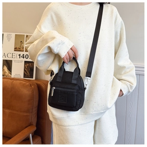 Fashionable black nylon crossbody bag with logo detail worn by a model in casual setting