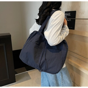 Detail of navy blue nylon tote bag with drawstring closure and large pockets on model