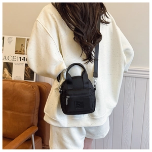 Detail of a black nylon mini crossbody bag with logo and adjustable strap worn by a model