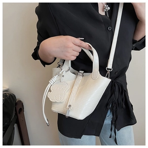 Detail shot of white faux crocodile bucket bag showing texture and small dog charm