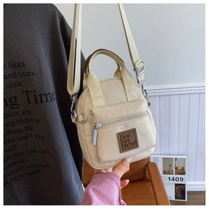 Detail of beige nylon crossbody bag with brand label and front zipper pocket