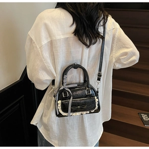 Detailansicht einer schwarzen Lackledertasche mit Schleife und Spitze auf weißem Hemd