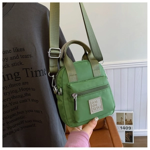 Detail of grass green nylon shoulder bag featuring a front zipper pocket and logo patch