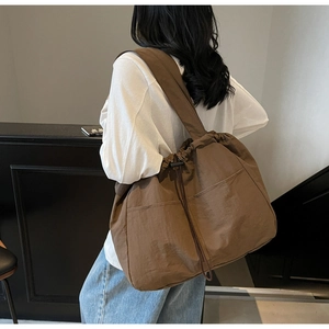 Detail view of the brown nylon drawstring tote bag worn over the shoulder by a model
