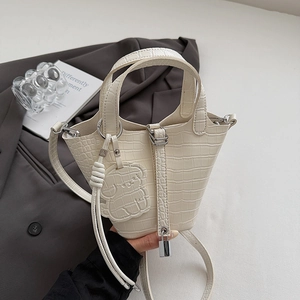 Close-up of cream-white crocodile texture bucket bag with puppy charm and metal lock