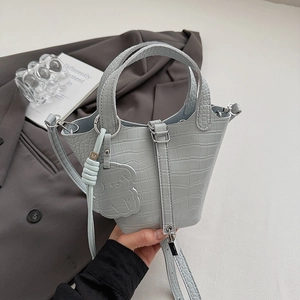 Detail of light blue faux leather bucket bag with crocodile texture and dog charm