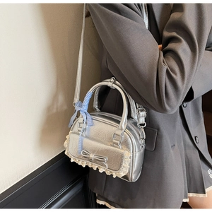 Detail der silbernen Metallic-Handtasche mit Schleife und Spitze getragen von Model