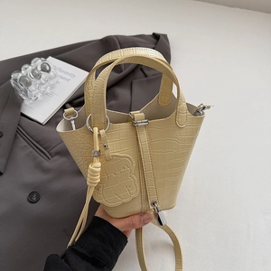 Detail of cream bucket bag featuring crocodile texture and a cute dog charm pendant