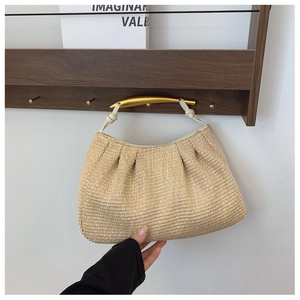 Detail of hand-woven straw bag featuring golden curved metal handle and beige leather knot