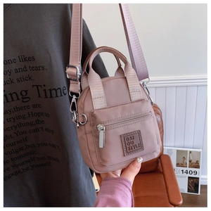 Detail of pink nylon crossbody bag with adjustable wide strap and square leather logo patch