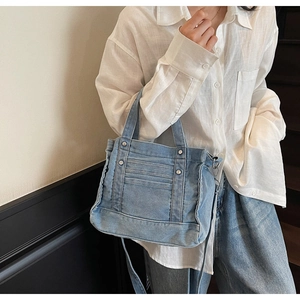 Detail of light blue denim crossbody bag with functional pockets and metal rivets
