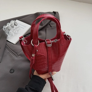 Detail of red crocodile textured bucket bag with metal clasp and bear charm on blazer