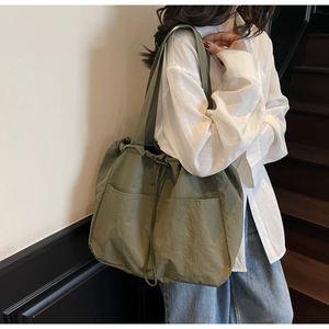 Detail view of army green nylon drawstring tote bag worn on shoulder by a model