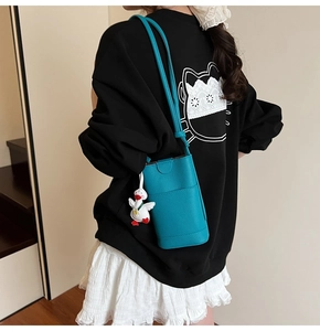 Détail d'un sac téléphone en cuir bleu paon avec un adorable pendentif canard en peluche