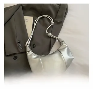 Detail of silver crescent dumpling bag with pleated texture and stylish knot shoulder strap
