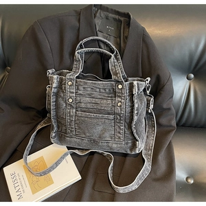 Detail of grey washed denim tote bag with rivets and detachable strap on black blazer